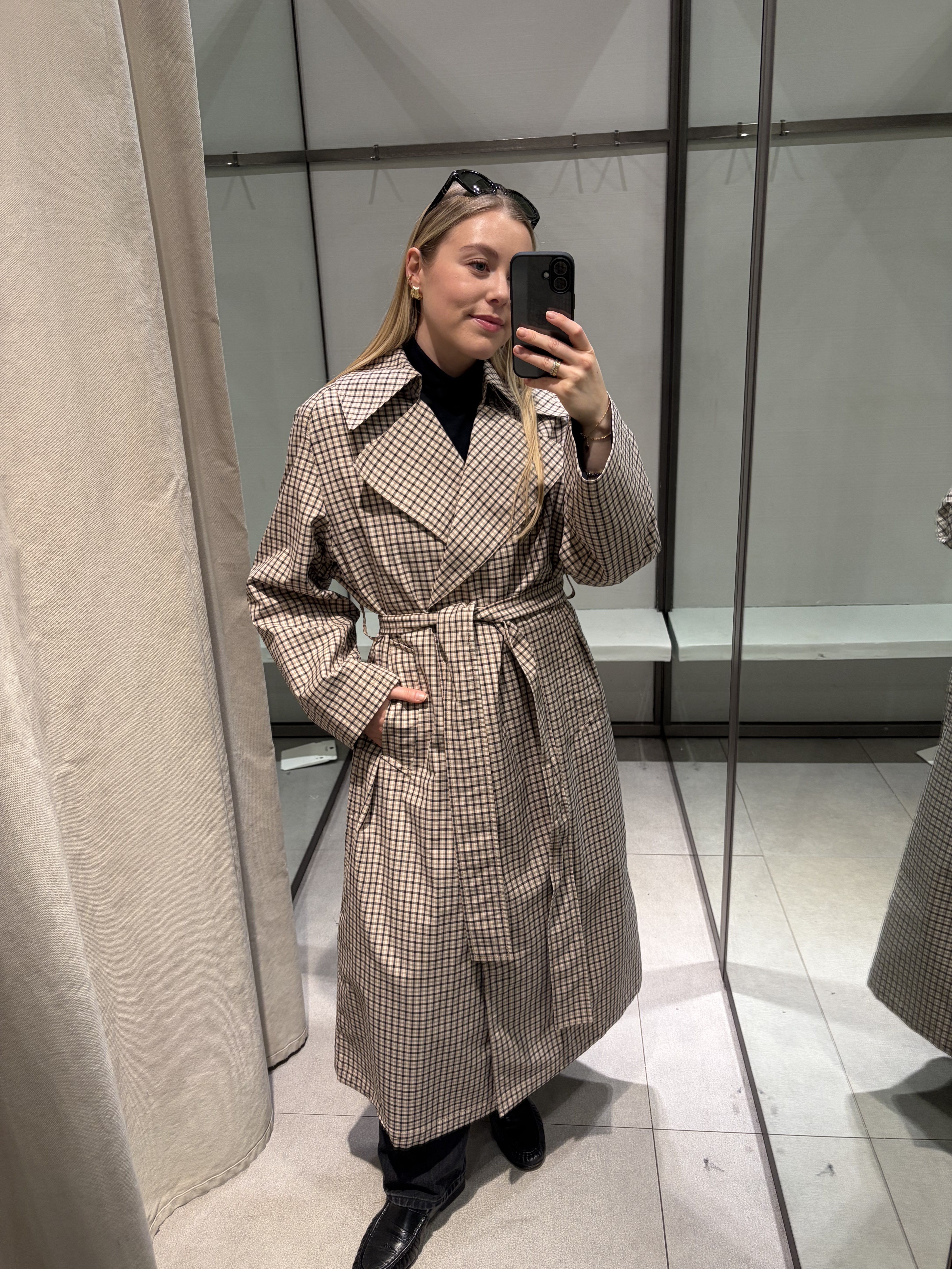 Woman wears check trench coat, black jeans and black loafers