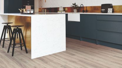 To illustrate can you paint laminate flooring – harrow grey oak laminate flooring in a modern kitchen with white island, dark bar stools, dark blue cabinets, gold splashbacks and white walls