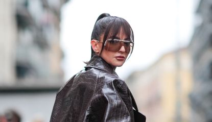 Alexandra Pereira wears sunglasses, a brown oversized leather jacket with crocodile patterns, a colored top with printed geometric patterns, brown underwear, brown tights, outside Missoni, during the Milan Fashion Week - Womenswear Fall/Winter 2024-2025 on February 24, 2024 in Milan, Italy.