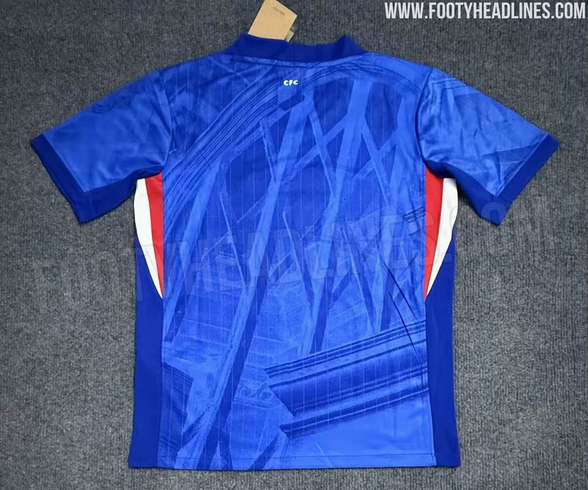 A sharply patterned blue top with a white tick on the left breast and a small circular logo with a blue lion on the right, a red and white stripe down the sides and a sharp pattern covering the back