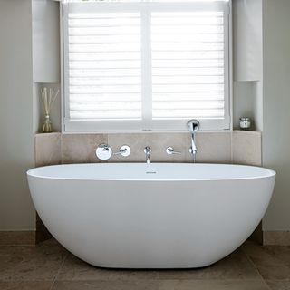 White oval bathtub in front of window with white wooden blinds