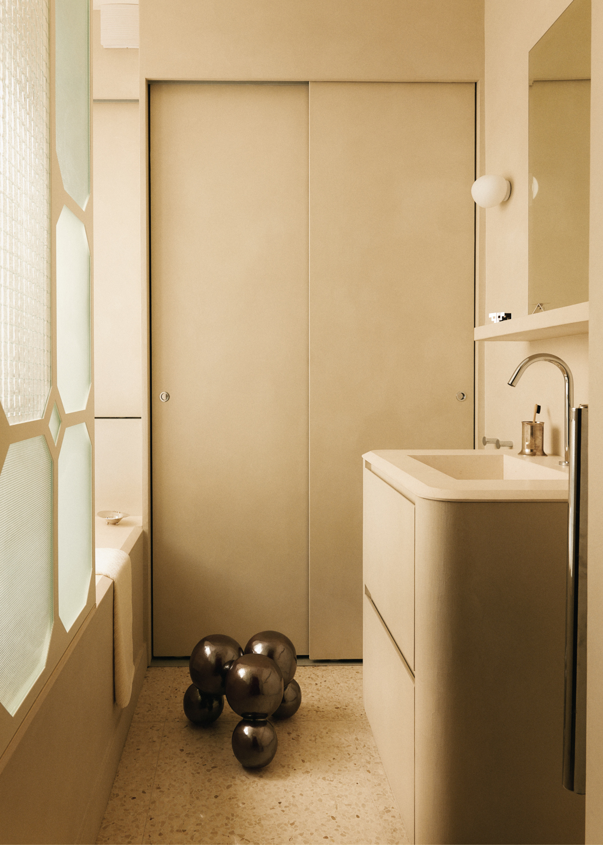A simple bathroom with sliding doors, a bubbled stool, a white sink, and silver fittings