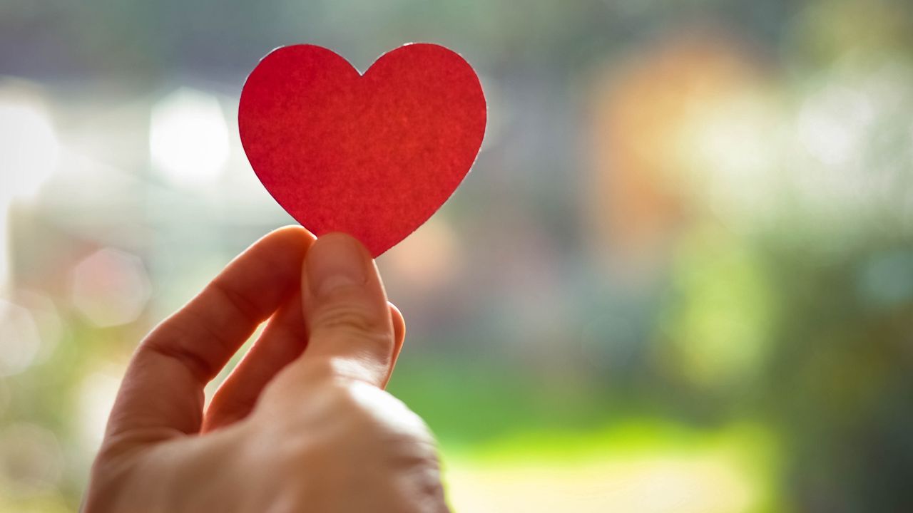 Fingers hold up a red paper cutout of a heart.