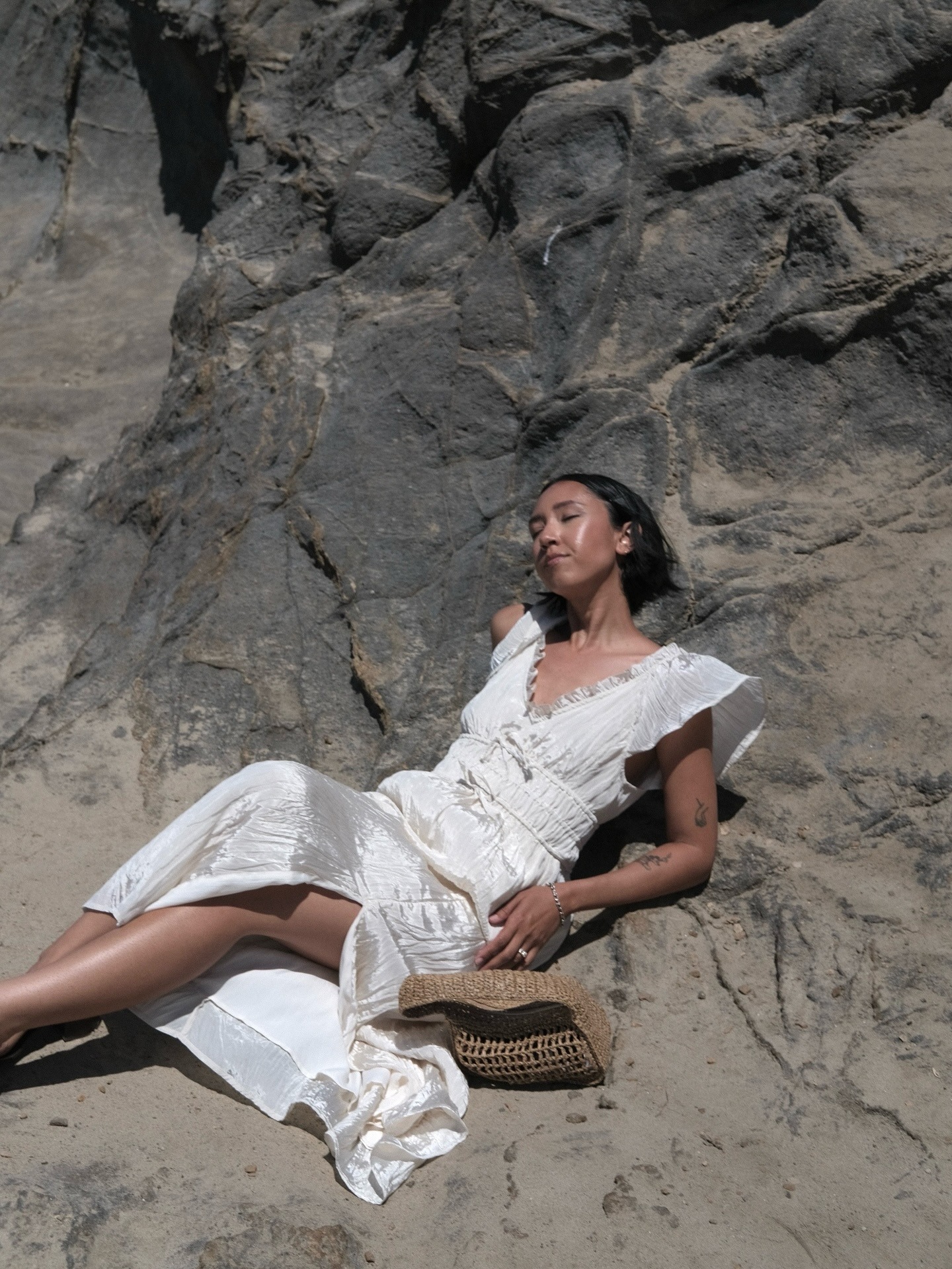 Woman on beach wears white dress and raffia bag