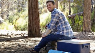 best camping coolers: man sat on hard cooler