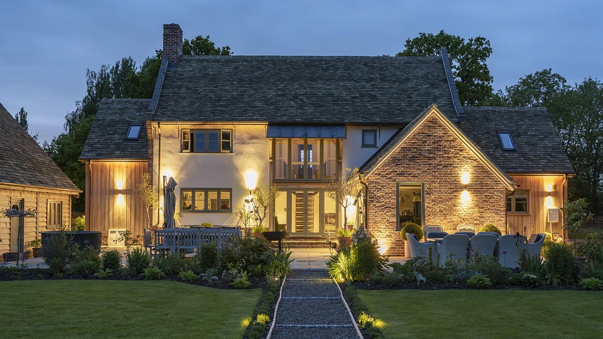 View of a traditional oak framed cottage at dusk with exterior wall lights creating a warm glowing ambience