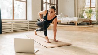 Woman doing Pilates at home using laptop for workout classes on yoga mat