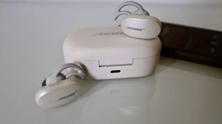 The Bose QuietComfort buds in white next to their case on a white surface.