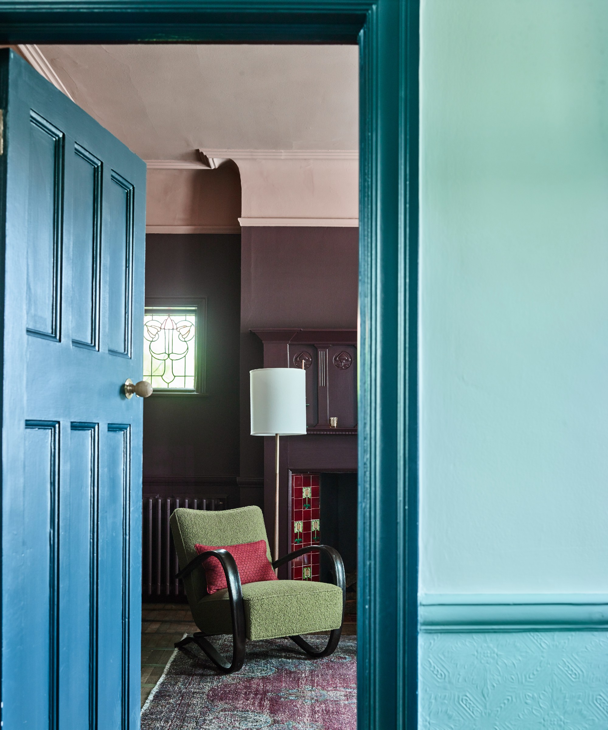 A hallway painted in three tones of blue with the door open to the purple and pink living room