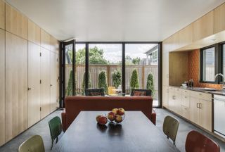 A kitchen with wooden cabinets, black wooden dining table and orange sofa