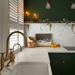 kitchen with white and green wall golden tap candles on shelf and frame on counter with fruit