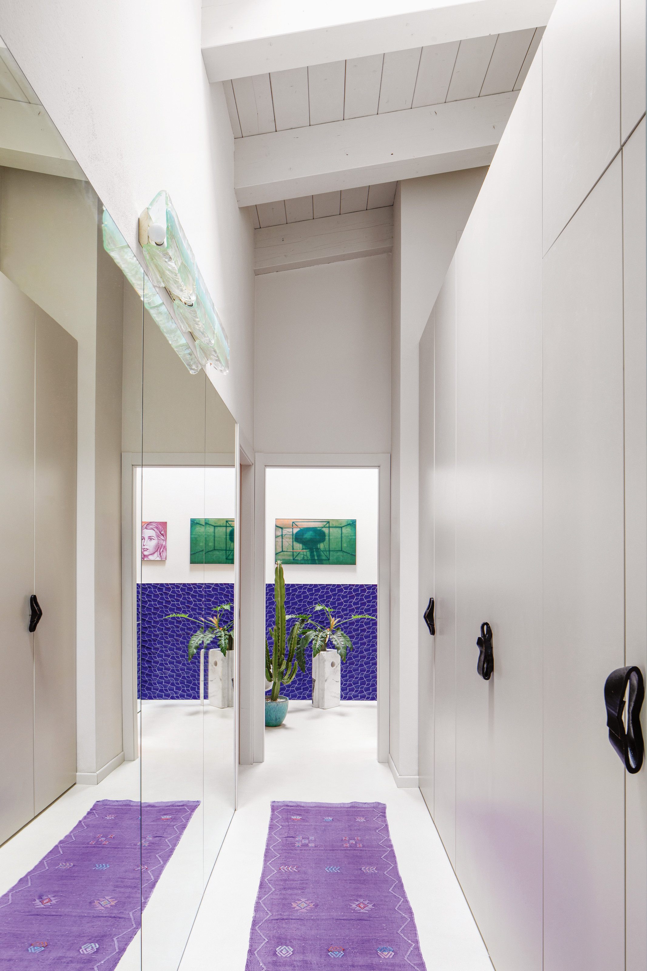 White hallway with mirrors along one wall, purple runner, blue tiles at the end of the hall