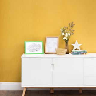 A hallway with a white sideboard against a yellow wall
