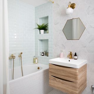 bathroom with white hexagonal designed tiles wall bathtub wash basin wooden drawer and hexagon mirror on wall