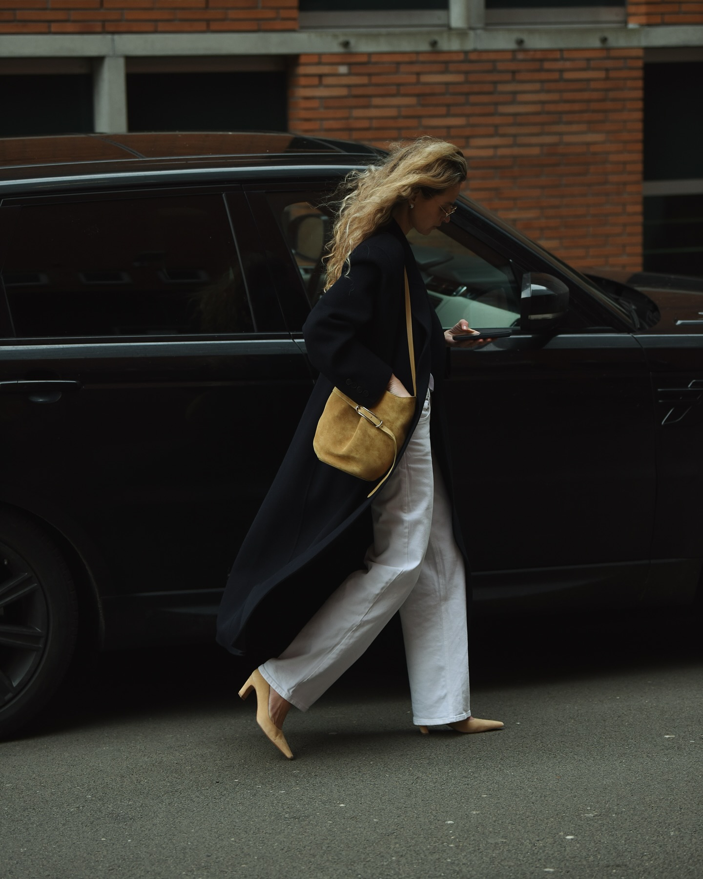 Anouk wears a black coat, white jeans, tan heels, and a tan suede liffner bag.