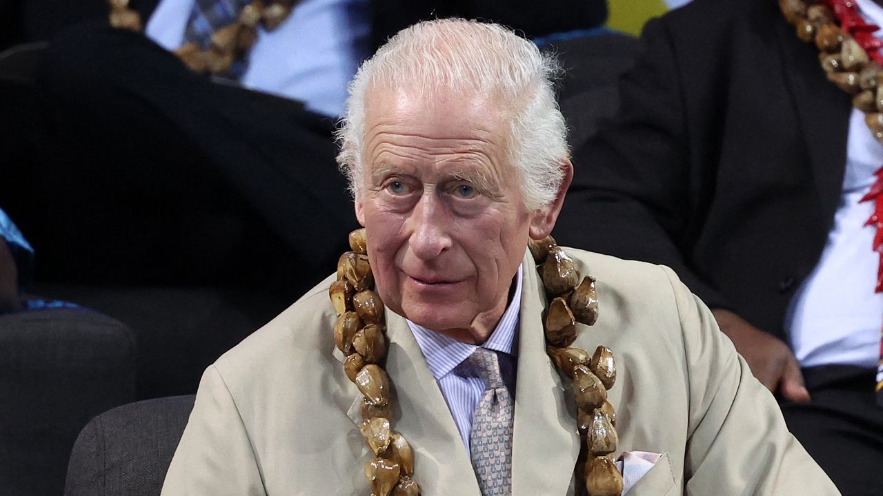 King Charles wears a light linen suit with a purple tie and white suit while looking sombre