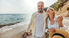 A happy, confident, retired couple strolls on a beach.