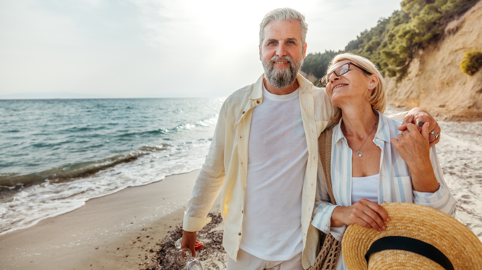 A happy, confident, retired couple strolls on a beach.