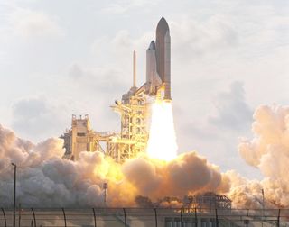 space shuttle Endeavour launching from the pad with white clouds in background