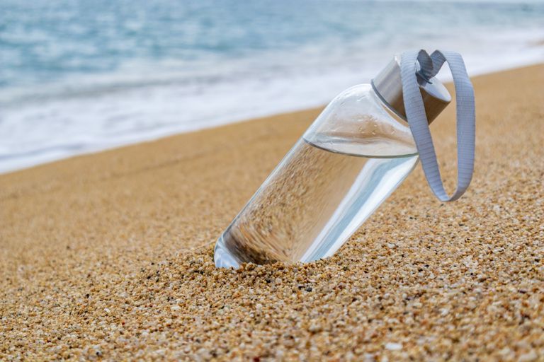 Glass reusable water bottle bottle filled with water on the beach with metal stopper, Best reusable water bottle