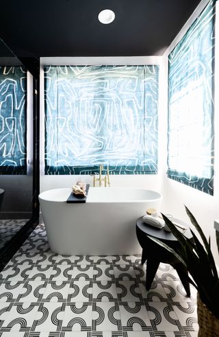 black and white bathroom with mono floor tiles, white bath and blue linear blinds
