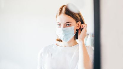 woman wearing mask looking at herself in the mirror