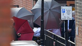 Staff use umbrellas to shield an individual wheeled to an ambulance parked outside the rear entrance of King Edward VII's Hospital in central London on March 1, 2021, where Britain's Prince Philip, Duke of Edinburgh has been staying.