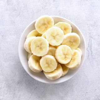 Banana slices in bowl over stone background.