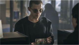 Tom Holland holding a dollar bill with "I have a gun" written on it in 'Cherry'.