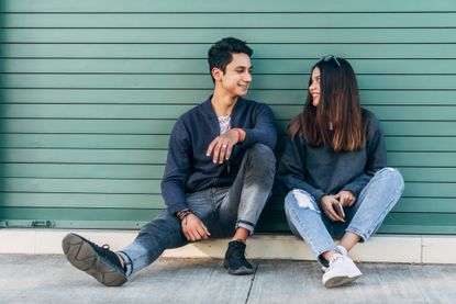 YOUNG COUPLE SITTING AND LOOKING INTO EACH OTHER'S EYES WHILE CHATTING WITH SMILING FACES