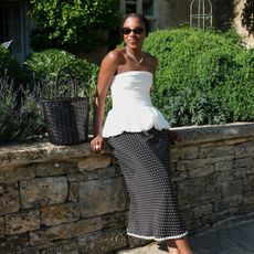 Woman wears white strapless top, polka dot skirt and woven leather bag