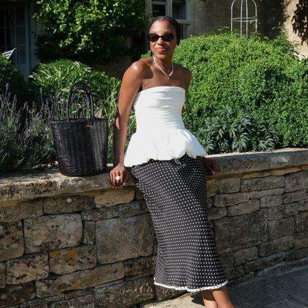 Woman wears white strapless top, polka dot skirt and woven leather bag