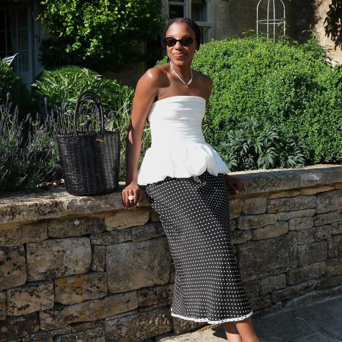 Woman wears white strapless top, polka dot skirt and woven leather bag