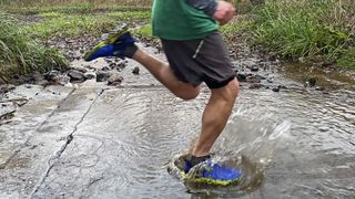 Trail runner wearing Inov8 TrailTalon all-terrain running shoes, running through a shallow stream