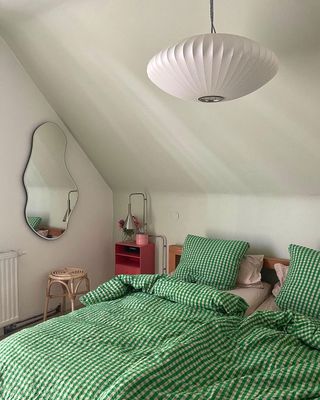 Gingham green sheets in small bedroom with wavy wall mirror and dark table lamp