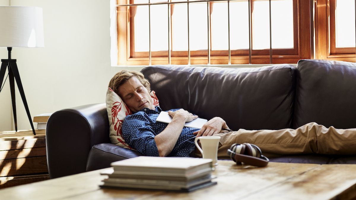 A blonde man wearing a blue shirt takes an afternoon nap on his brown leather couch during a summer heatwave