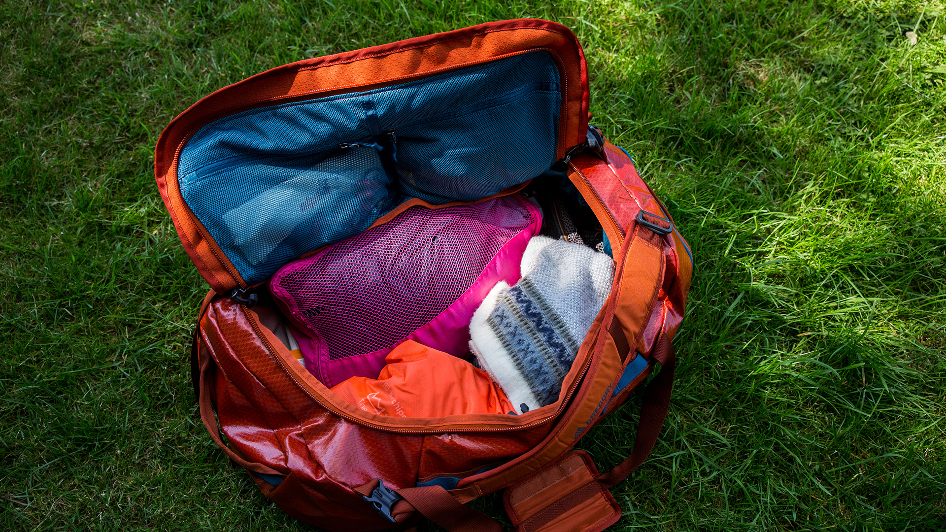 A Gregory Alpaca 60 duffel bag on a patch of grass. The top of the bag is open and there are clothes packed inside.