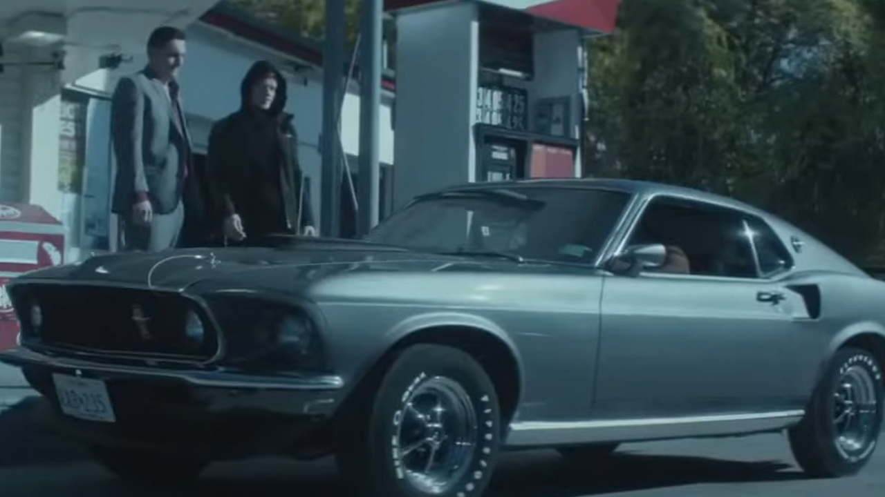 A silver mustang from the side, parked at a gas station in John Wick