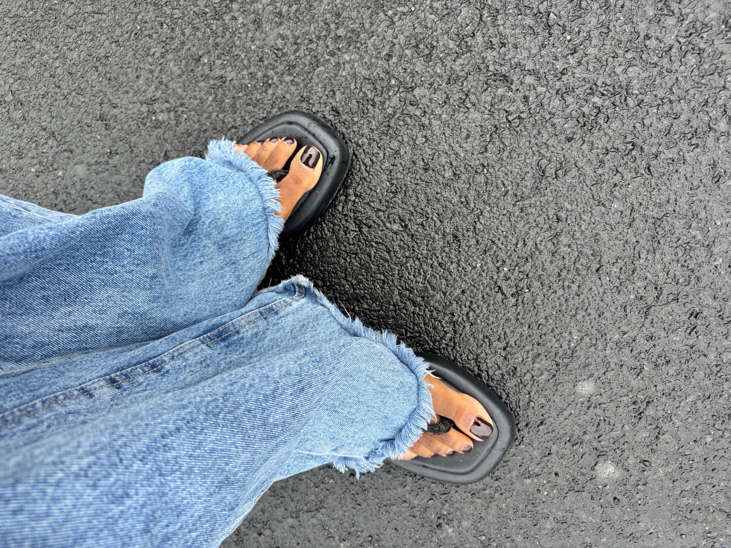 black sandals and blue jeans with toes wearing Clinique's Black Honey Nail polish