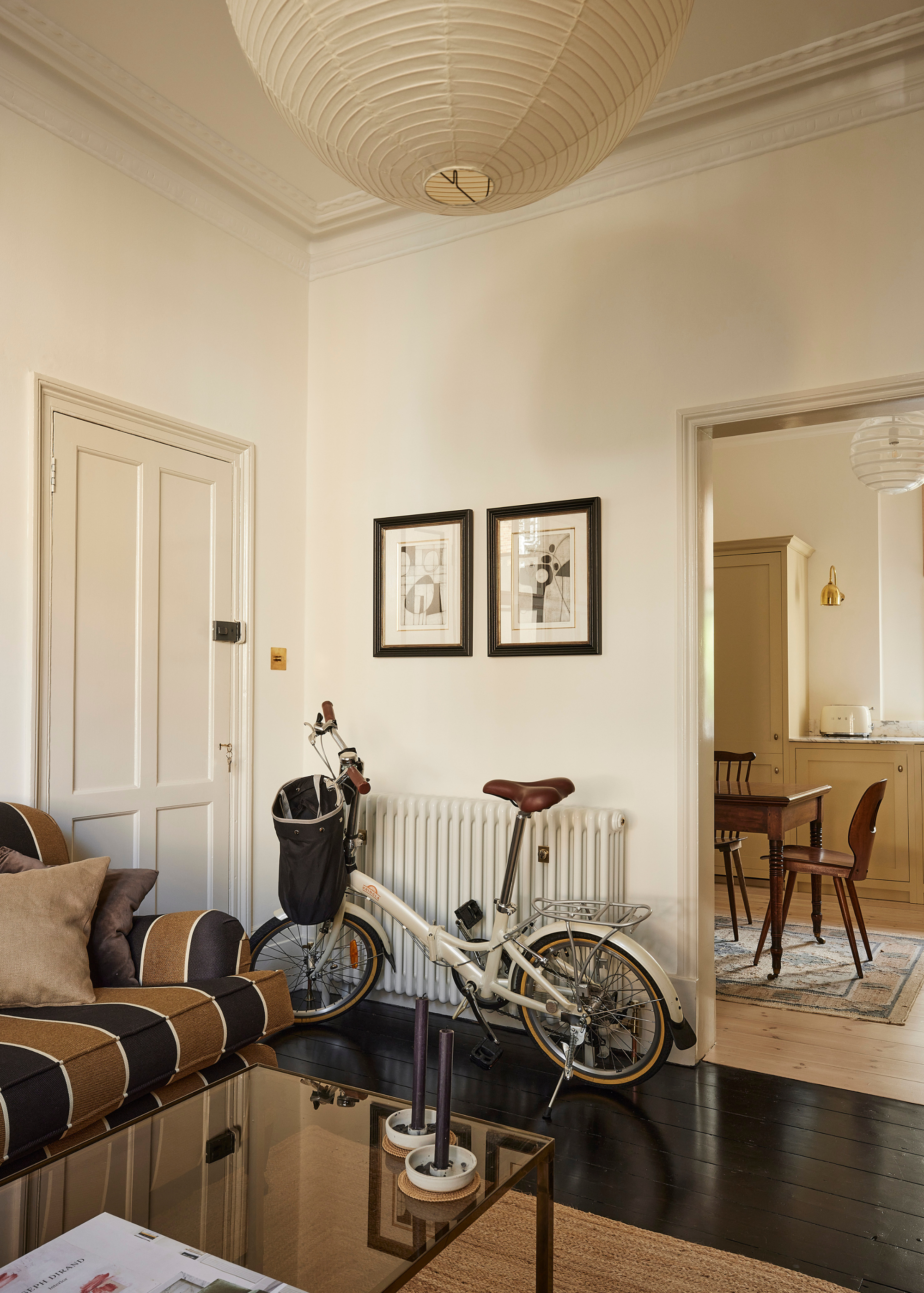 A living room with a striped couch, a glass coffee table, a set of candle holders, a paper lantern, and a bicycle