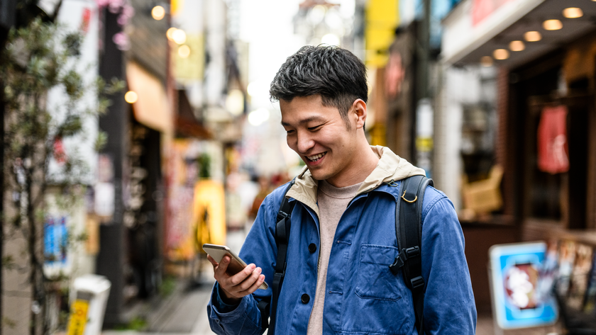 Man holding a phone wearing a backpack down a street for Nomad eSIM