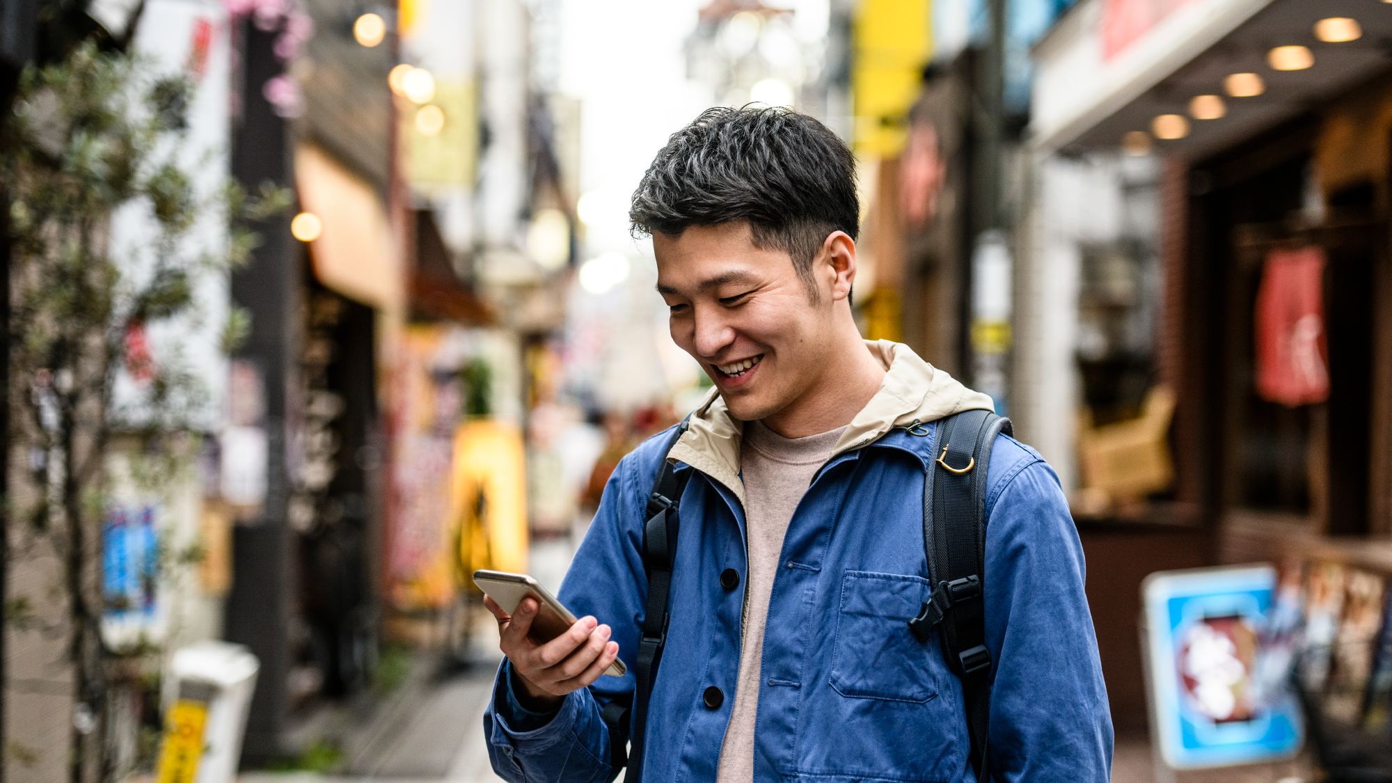 Man holding a phone wearing a backpack down a street for Nomad eSIM