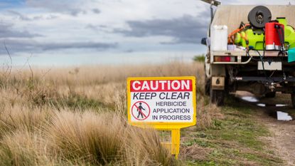 A sign warning about herbicide on the edge of a field with a truck in the background 