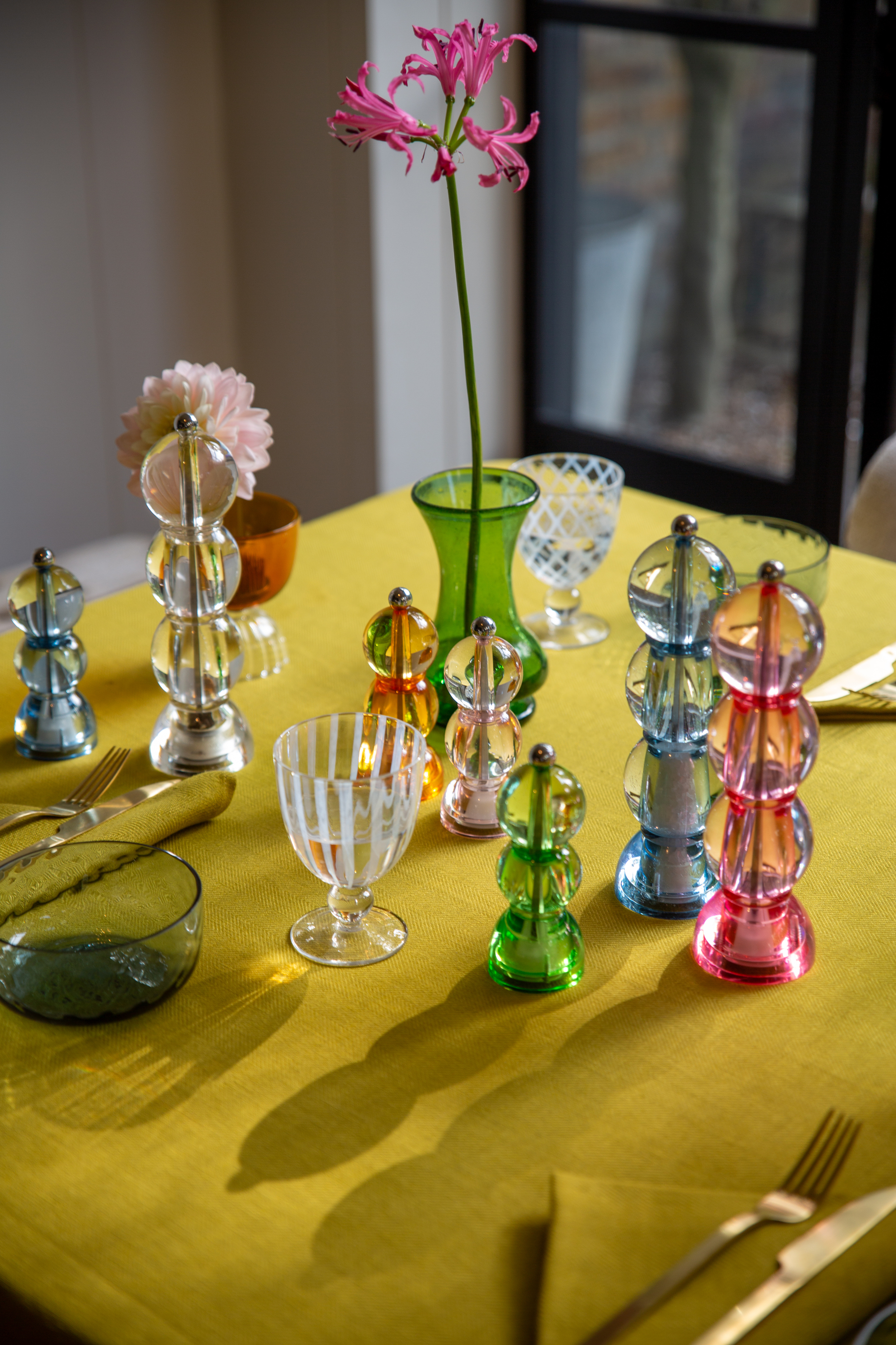 table set with colorful addison ross salt and pepper mills, chartreuse tablecloth, striped glassware, green vase with flower