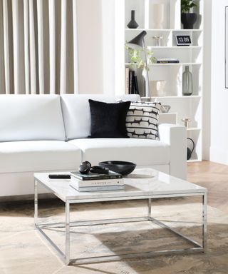 A monochrome living area with a white couch, coffee table, and bookcase