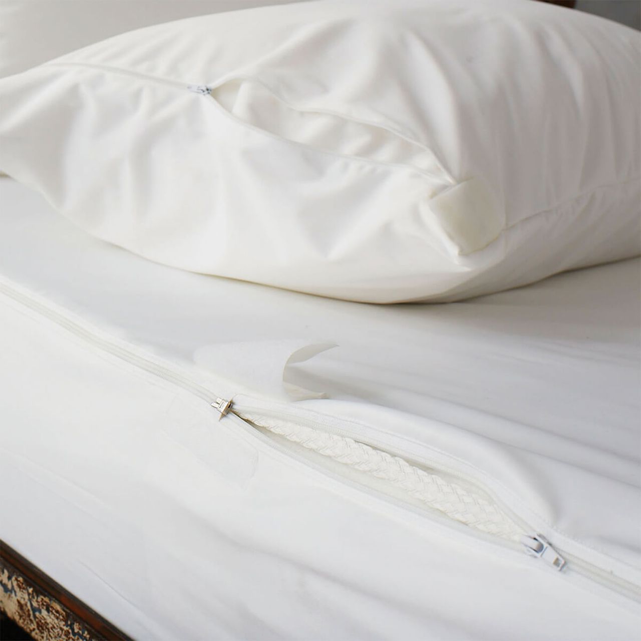 Soak &amp; Sleep Anti Bed Bug Mattress Encasement on a mattress with two zips pulled apart to expose the mattress, with a pillow sat on top.