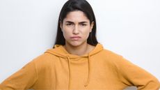 A young woman has her hands on her hips, looking annoyed.