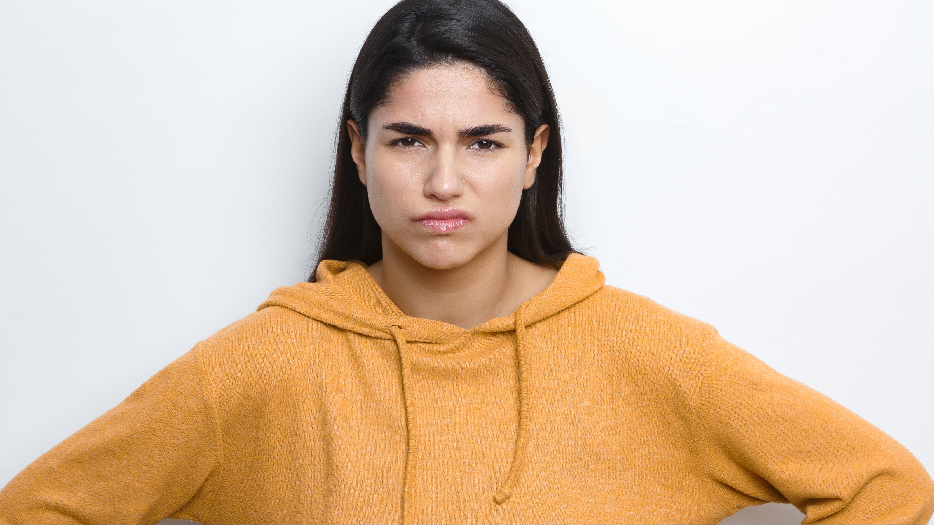 A young woman has her hands on her hips, looking annoyed.