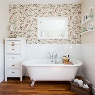 bathroom with bird print wallpaper ans white tile wall bathtub wooden floor and white cabinet