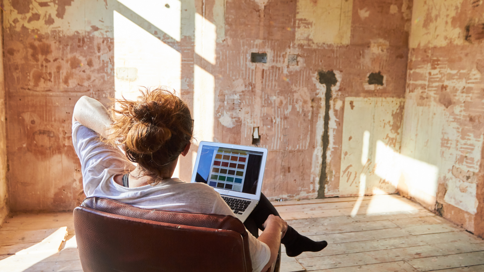 woman sat in room with bare walls and floor looking at laptop